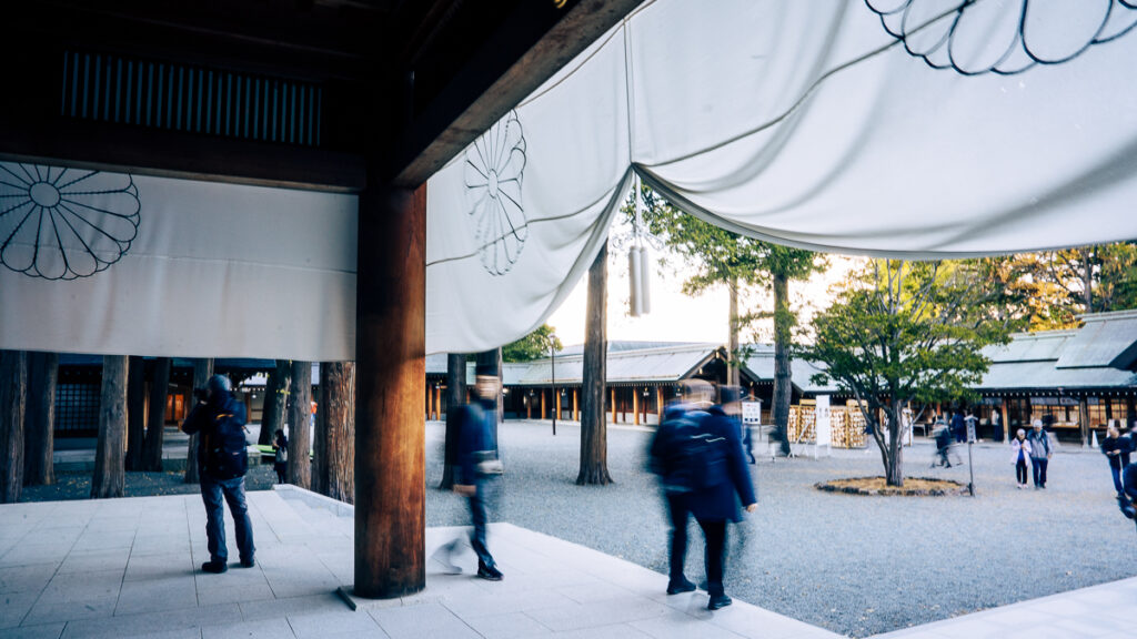People gathered in the courtyard seen from inside the sanctuary under white imperial crest banners.