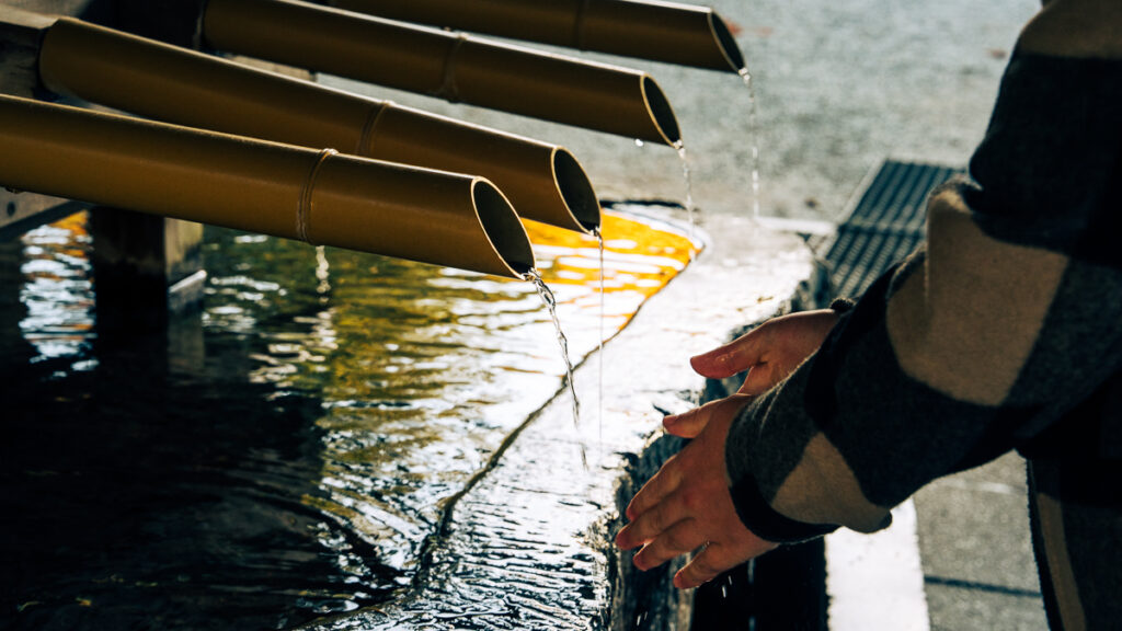 Visitor washing hands at the temizuya water pavilion for purification before entering the holy area at Hokkaido-Jingu
