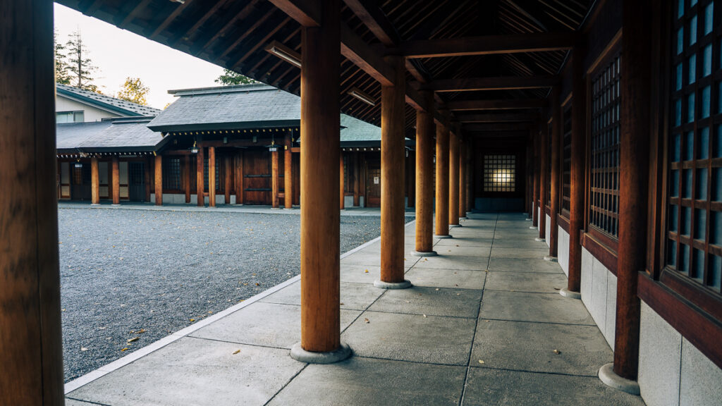 A wooden passageway between shrine buildings lined with tall columns in afternoon light