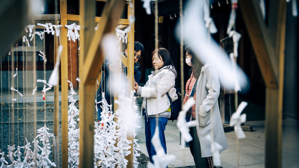 A woman reads her omikuji fortune at Hokkaido-Jingu while tied paper fortunes hang blurred in the foreground