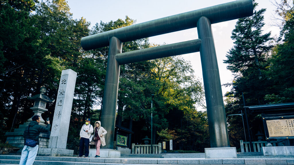 Visitors pause at the large wooden torii gate at Hokkaido-Jingu in Sapporo during a calm autumn afternoon