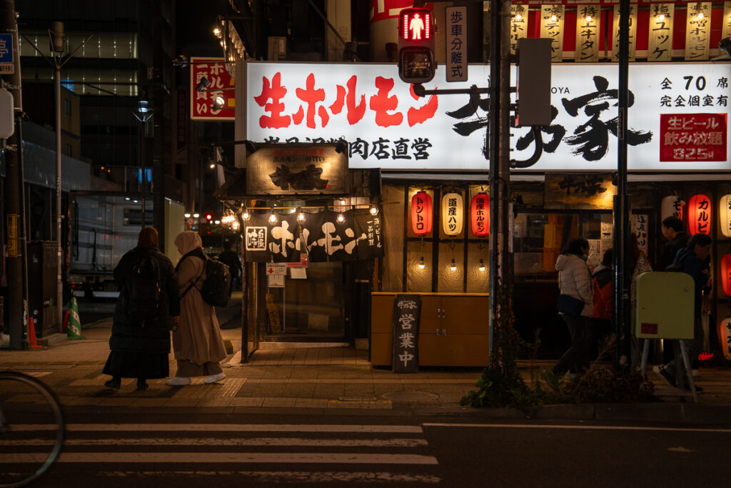 People bundled in coats outside a lantern-lit restaurant in Sapporo, Japan, warm red and white lights glowing on a cool autumn night.