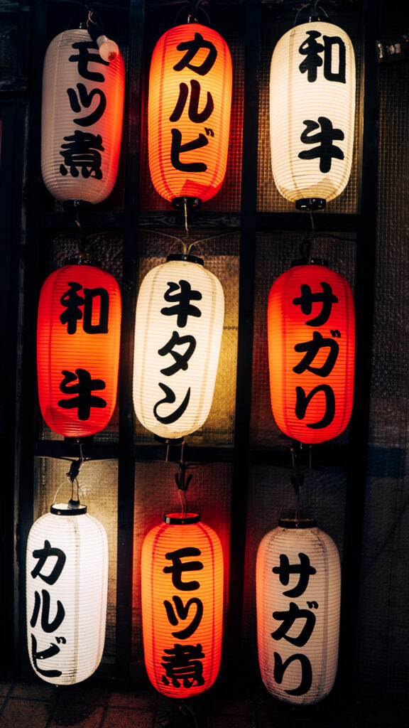 Vertical rows of red and white lanterns listing food offerings like wagyu beef, beef tongue, and boiled offal in Sapporo, Japan.