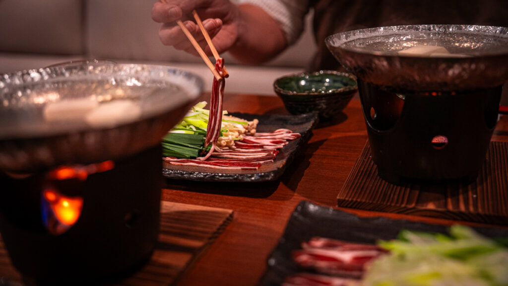 Chopsticks lifting a slice of raw sika deer meat before cooking.