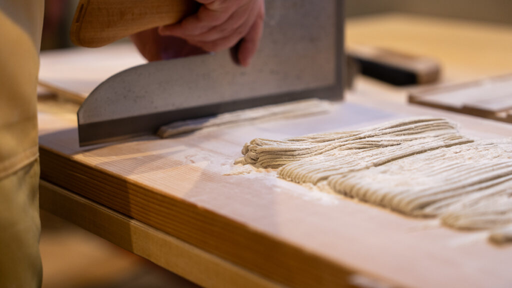 Strips of freshly cut soba noodles arranged neatly beside the dough.