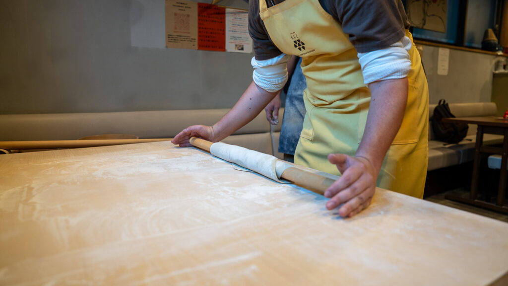Mac rolls soba dough onto the large pin to shift its position on the table.