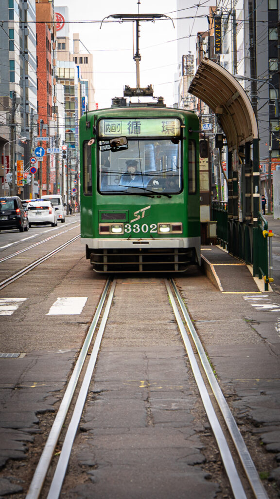 Green Sapporo streetcar number 3302 seen head-on on city tracks.