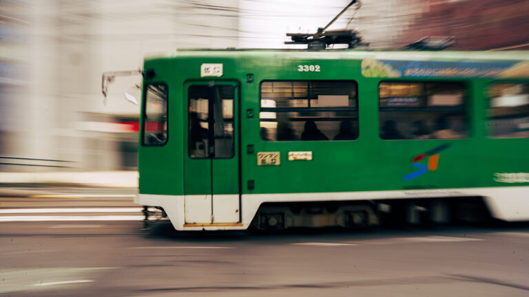 Blurred green streetcar moving through downtown Sapporo with a long shutter speed.