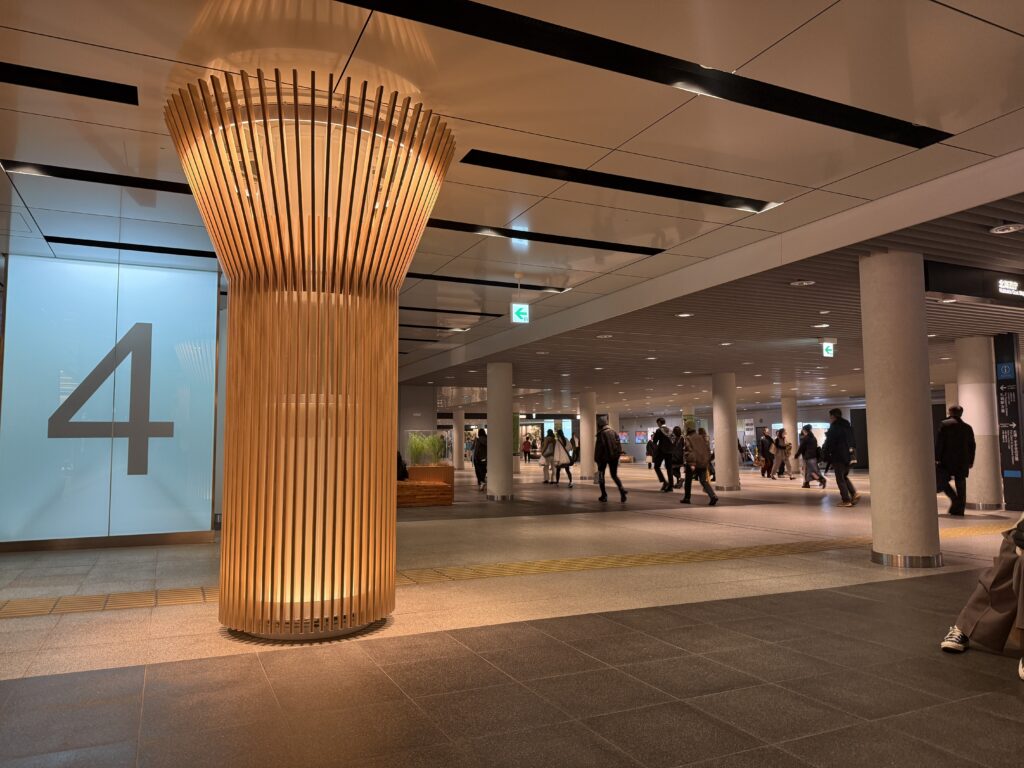 Wide underground shopping passage in Sapporo with a glowing decorative pillar as people walk by in a bright, clean transit space.