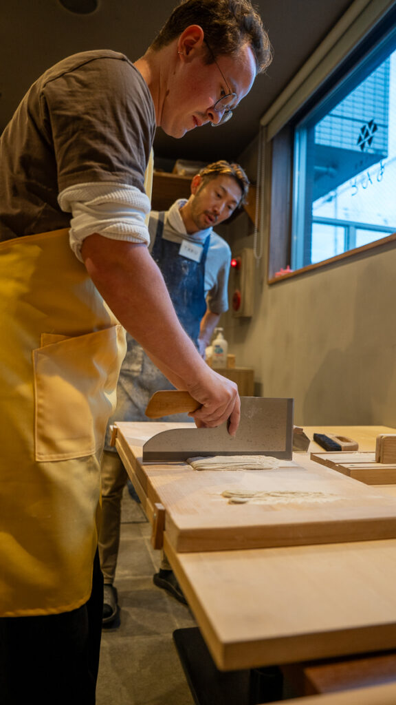 aku-san watches as Mac cuts noodles using a large soba knife in Sapporo.
