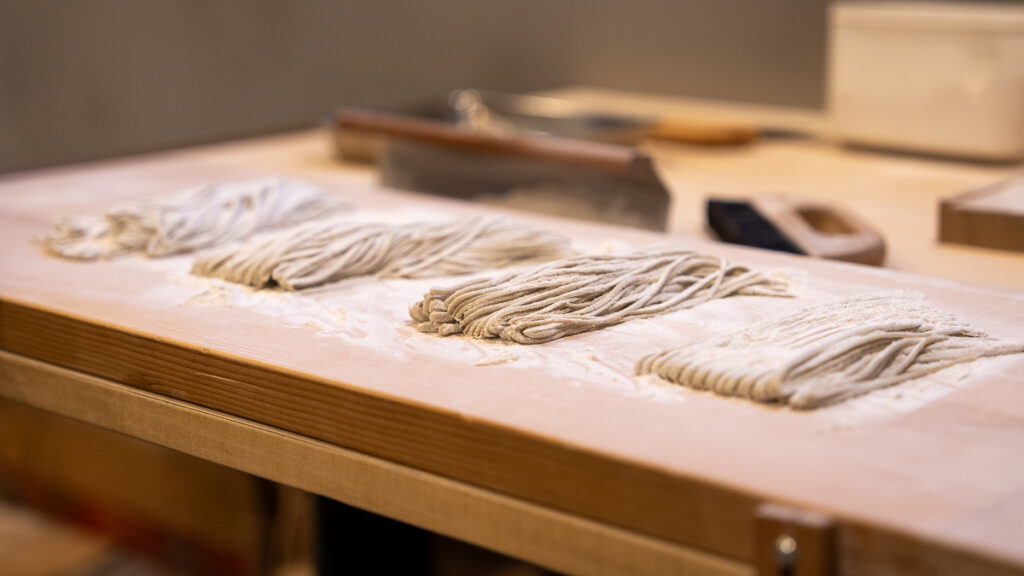 Side angle showing stacks of thin soba noodles on a wooden board.