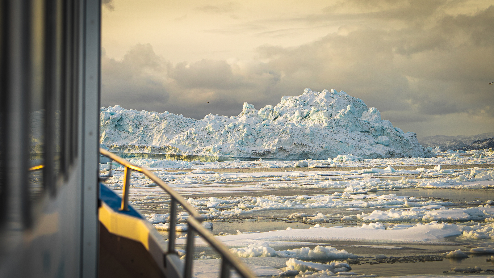 View from boat of ice-covered bay, iceberg in the distance, railing of the boat is visible