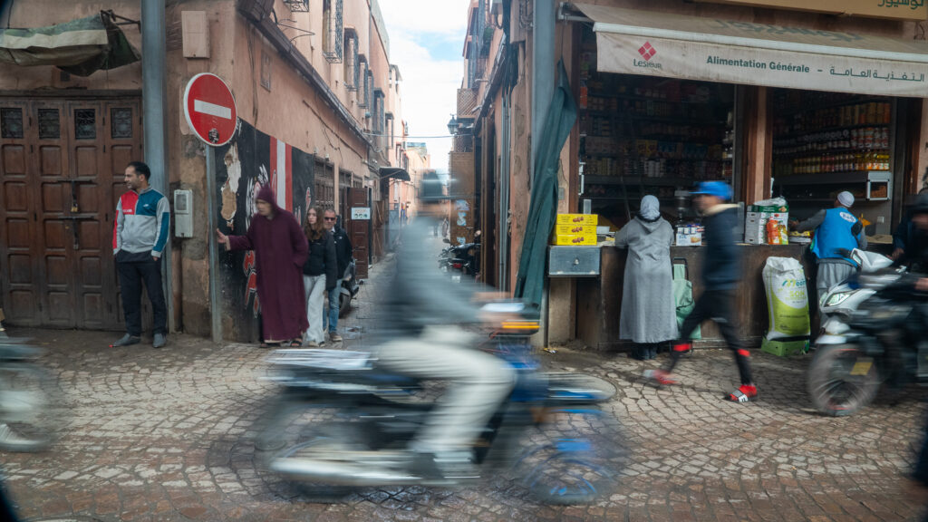 Long exposure of a busy Marrakech medina street with pedestrians blurred around a motorbike