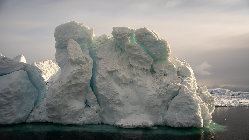 Deep glowing blue cracks in an iceberg floating on dark water in Disko Bay, Greenland.