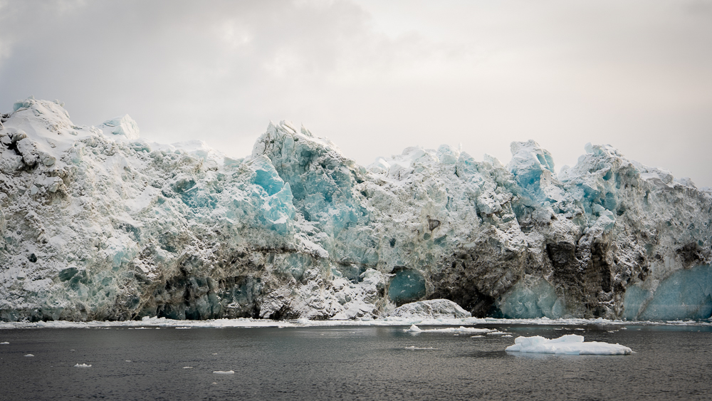 Highly textured iceberg displaying blue ice and brown sediment streaks.