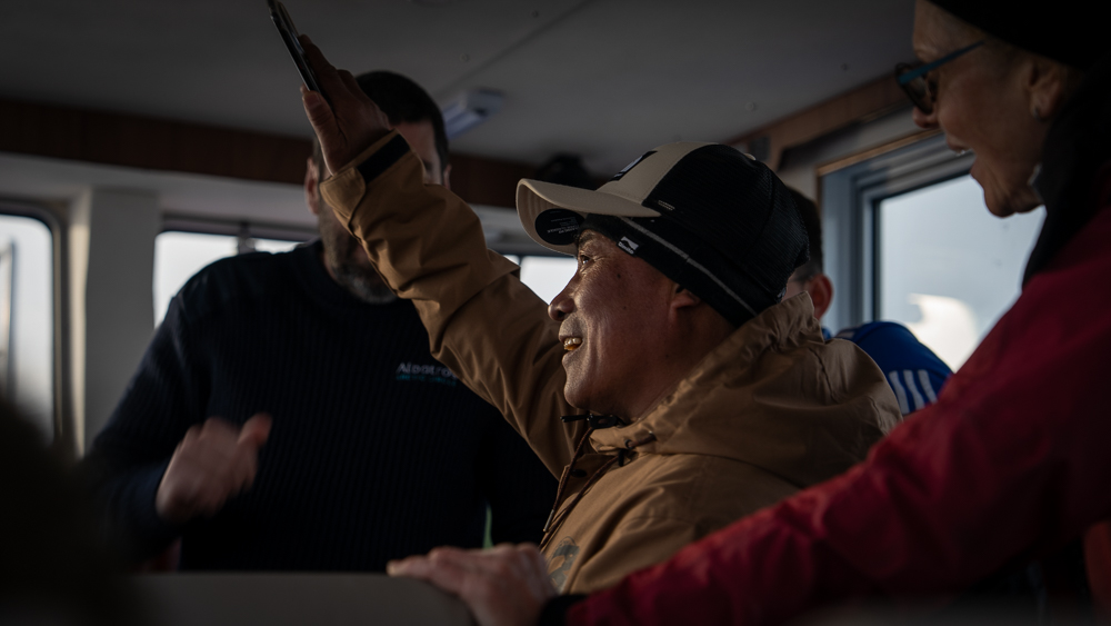 Man gesturing while telling a story inside an iceberg tour boat in Greenland.