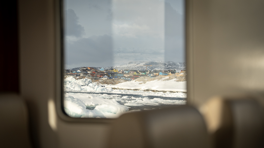 View from inside an iceberg tour boat in Disko Bay, Greenland, with colorful houses of Ilulissat visible through the window.