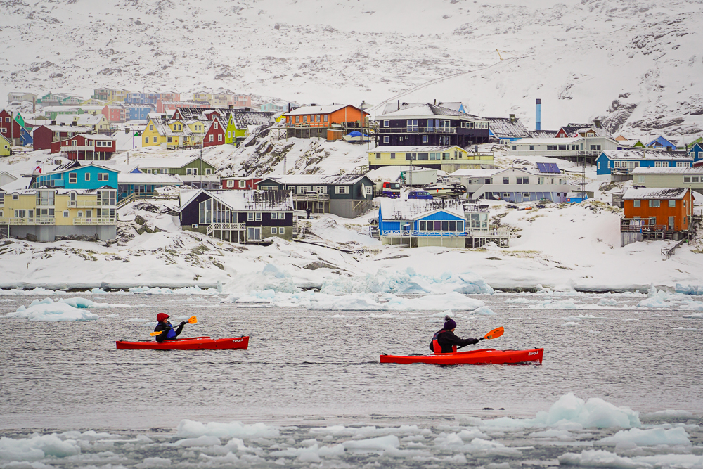 Kayakers paddling across Disko Bay with colorful Ilulissat behind them.