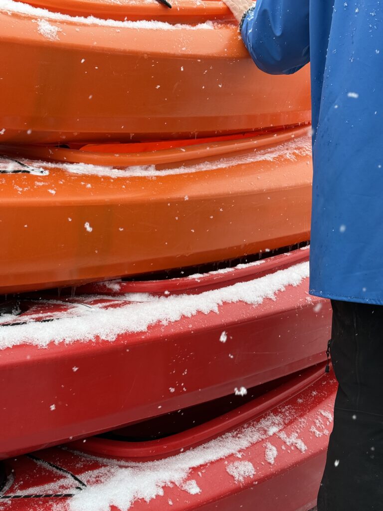 Close-up of stacked orange sea kayaks dusted with fresh snow in Ilulissat.