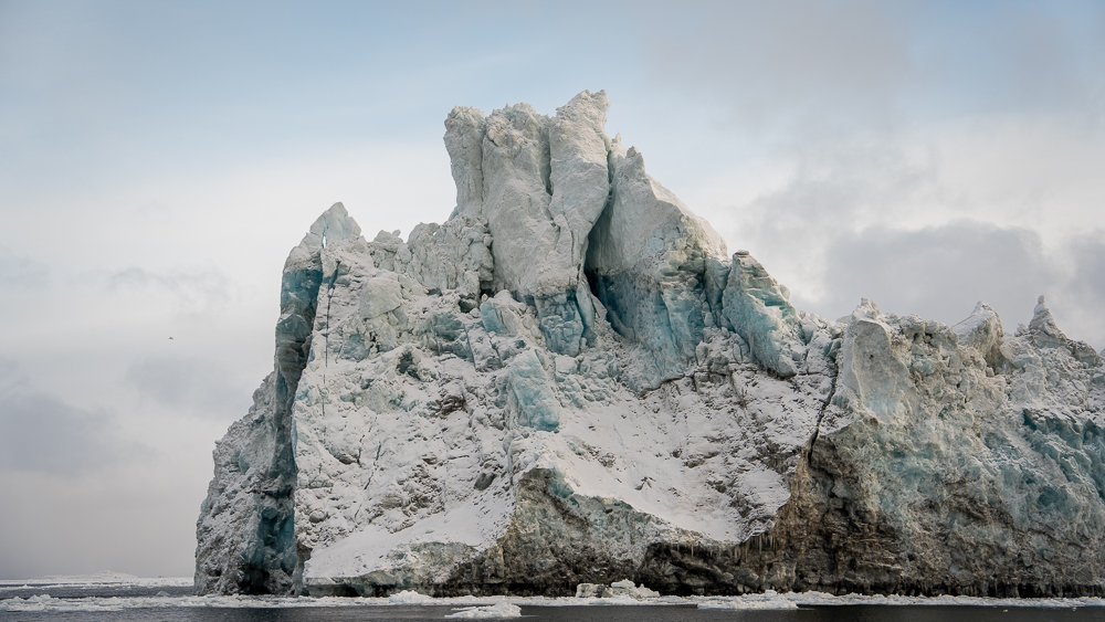 Towering iceberg with rounded peaks and bands of brown, blue, and white ice.