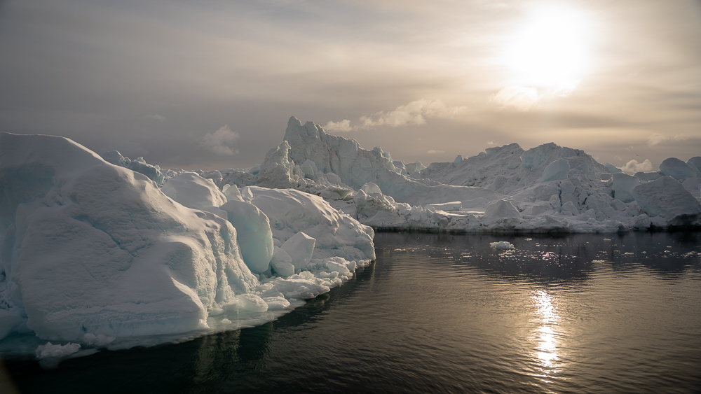 Two icebergs floating side by side in Disko Bay with sunset reflected on calm Arctic water.