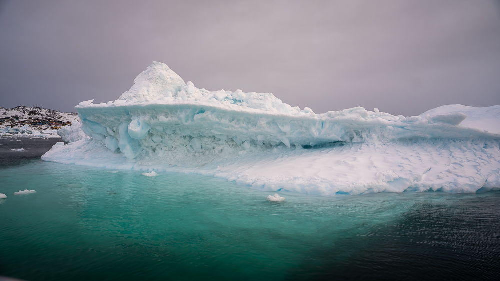 Aquamarine ice visible below the waterline of an iceberg floating in black Arctic water.