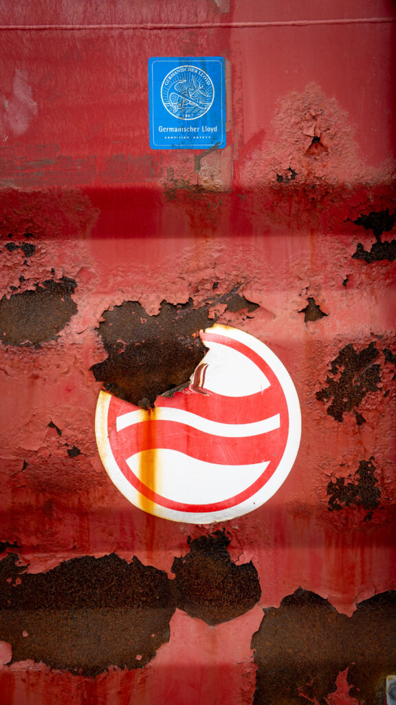 Close-up of a red Royal Arctic shipping container with chipped paint exposing rusted steel beneath.