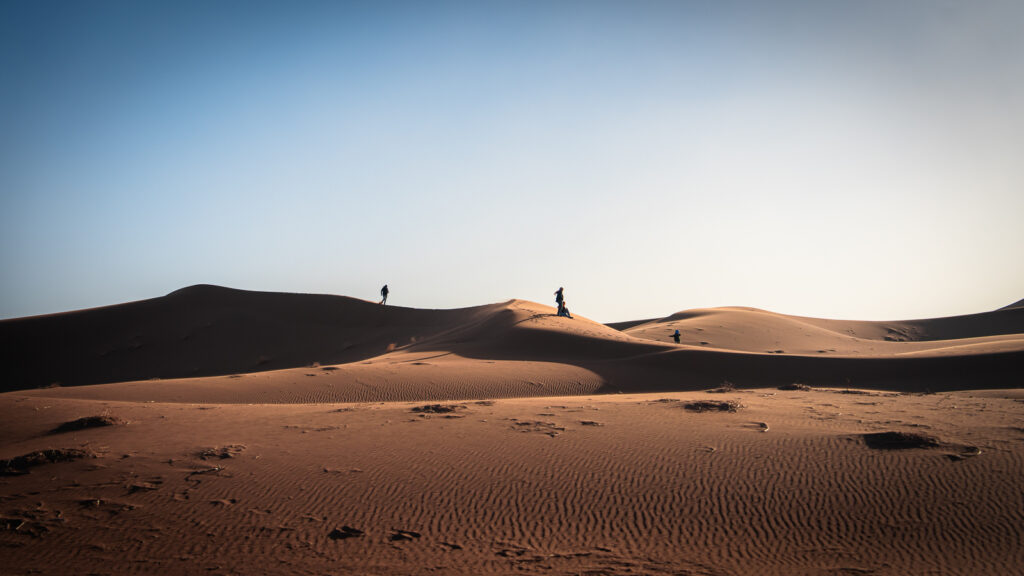 Small dunes in the Sahara Desert near Erg Chigaga with silhouettes of people standing on the ridgeline.