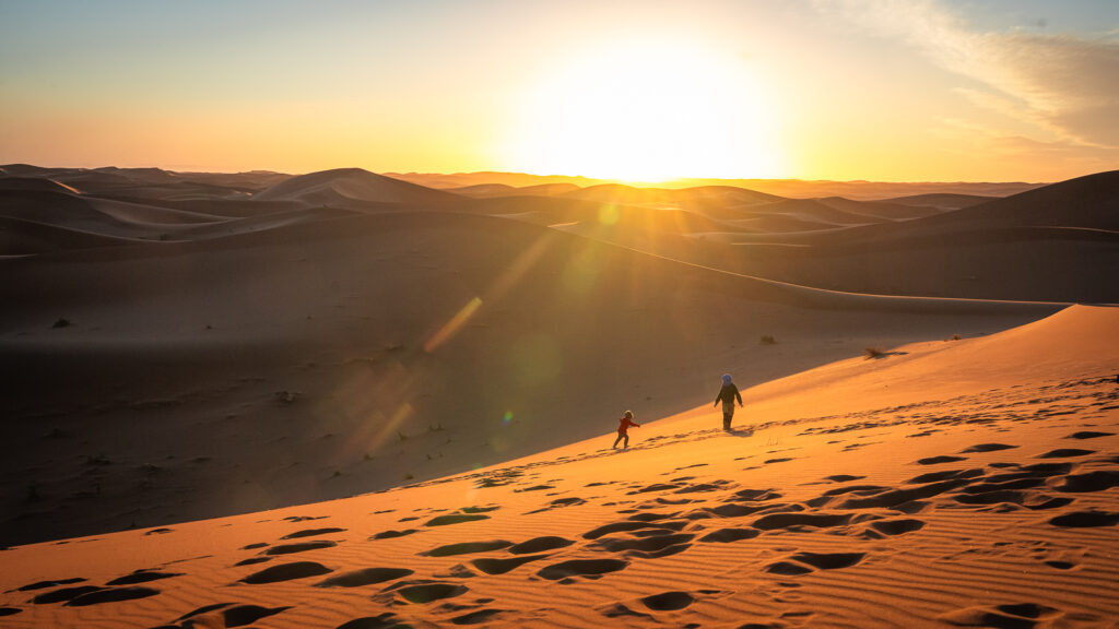 Silhouettes of a child and adult walking up a dune at sunset near Erg Chigaga.