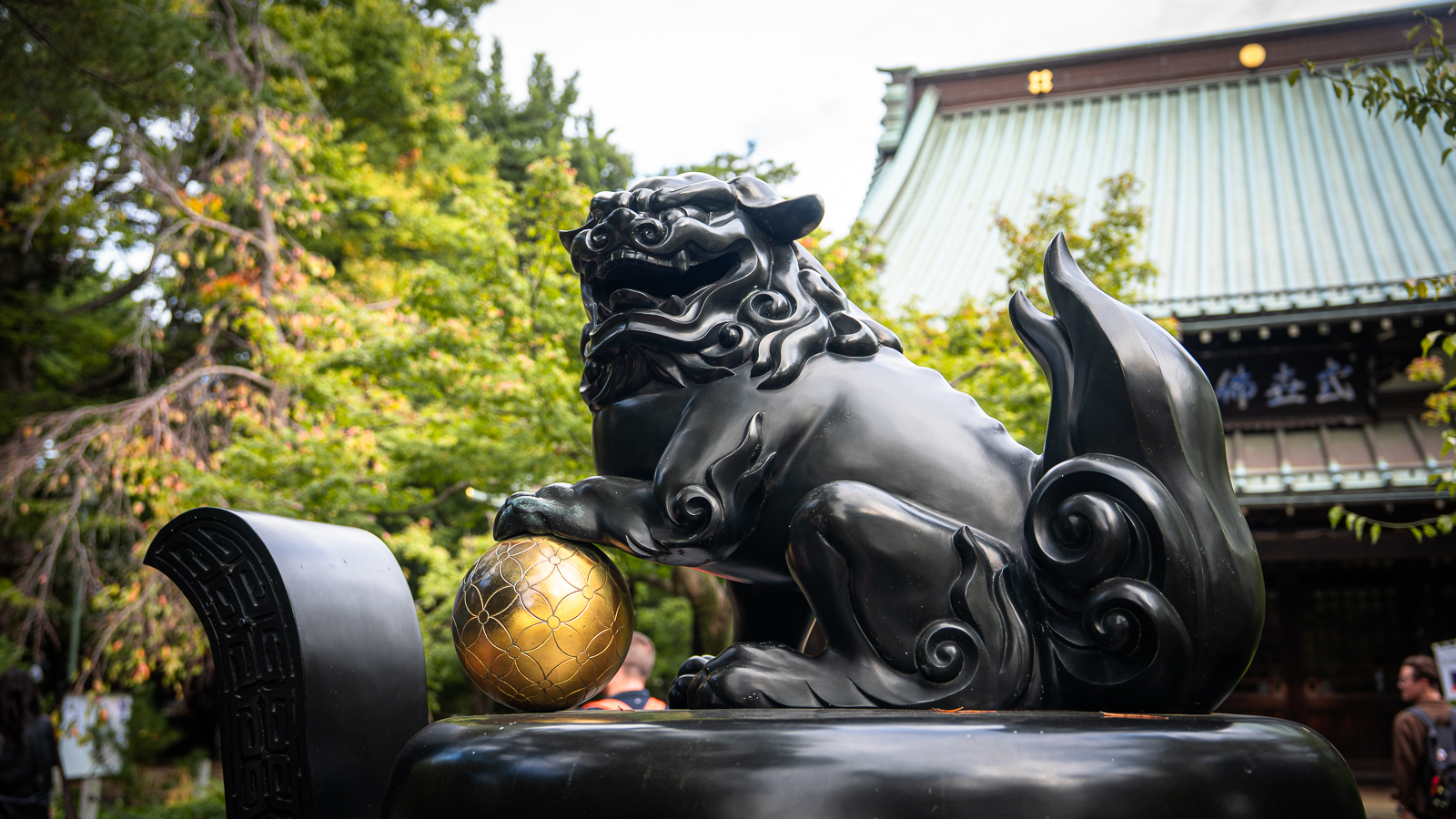 Lion-dragon guardian statue holding a gold ball along a tree-lined path at Gotokuji Temple.
