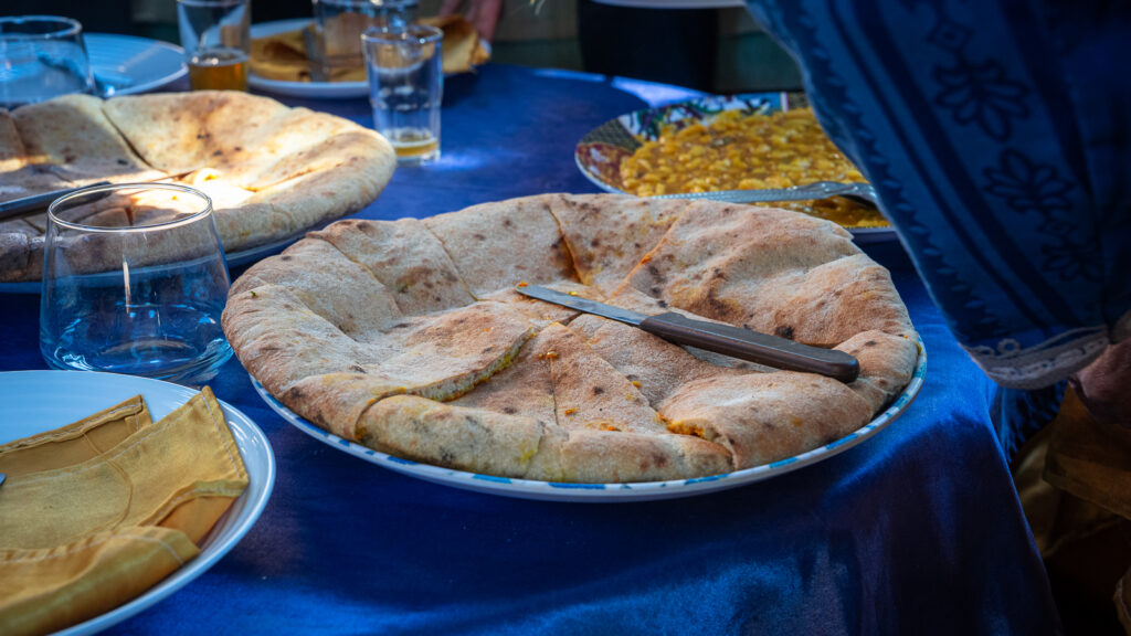 Berber pizza served on a plate with fava beans and table setting on a bright blue tablecloth at Auberge Kasbah Touareg in M’Hamid, Morocco.