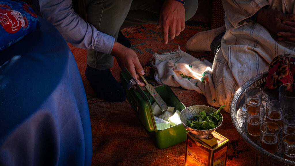 Close-up of hands breaking apart sugar inside a metal tin during Moroccan tea preparation at Auberge Kasbah Touareg in M’Hamid.