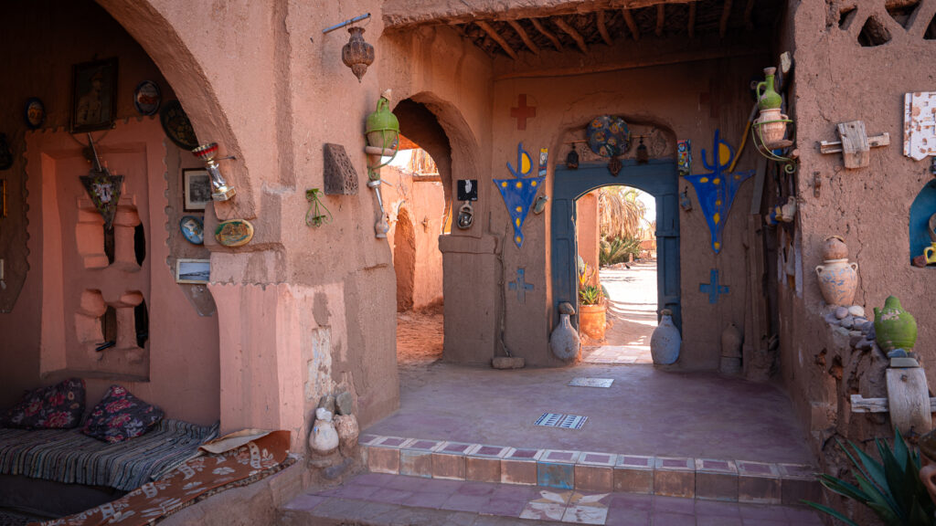 Entrance interior at Auberge Kasbah Touareg in M’Hamid decorated with blue Amazigh fertility symbols, clay pots, lanterns, and shaded archways.
