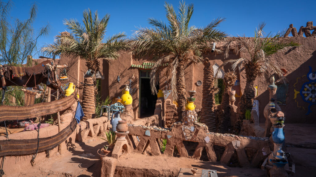 Guest rooms, palm trees, yellow pots, and clay decorative patterns inside the Auberge Kasbah Touareg compound in M’Hamid.