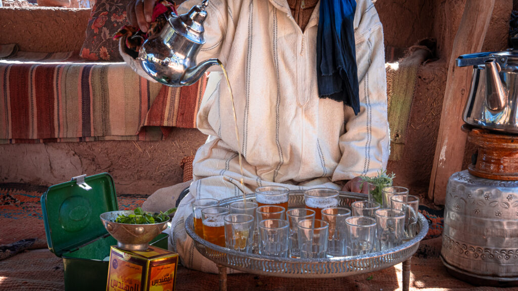 Close view of Moroccan tea pouring from a silver teapot into small glasses from height at Auberge Kasbah Touareg in M’Hamid.