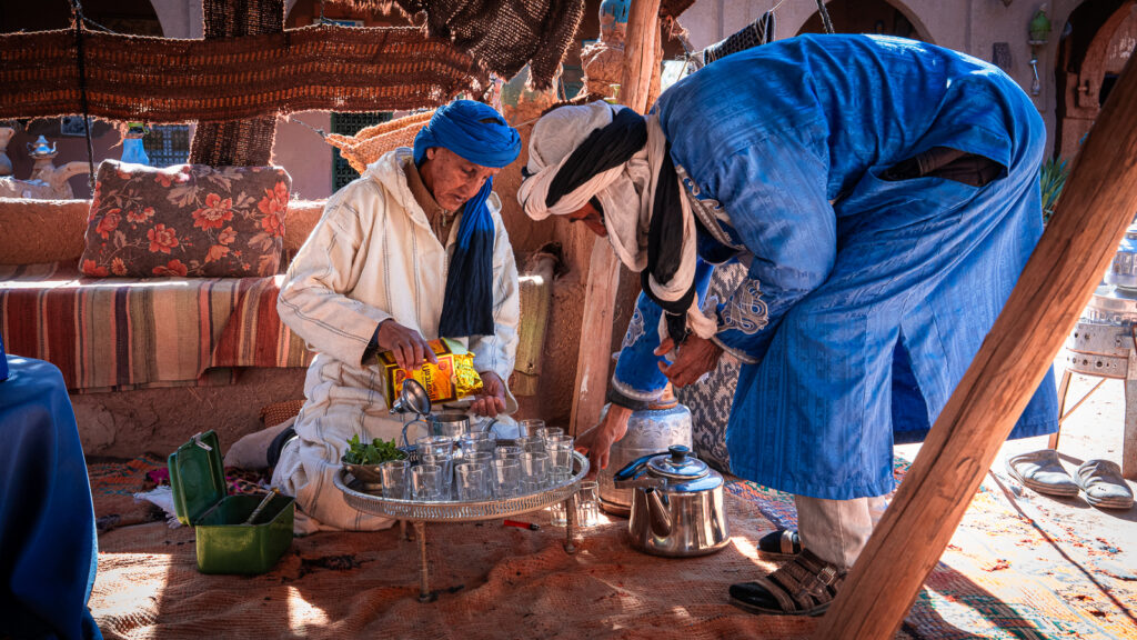 Two men in djellabas prepare Moroccan tea together inside the tent at Auberge Kasbah Touareg in M’Hamid, Morocco.