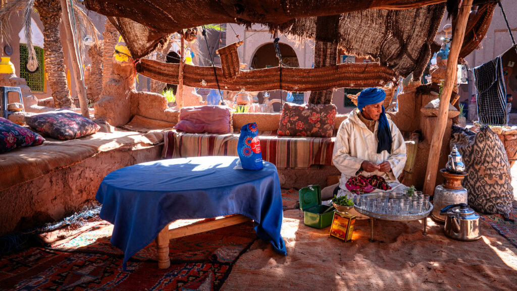 Interior of the tent seating area at Auberge Kasbah Touareg in M’Hamid with rugs, cushioned benches, and the tea host waiting as the tea steeps.