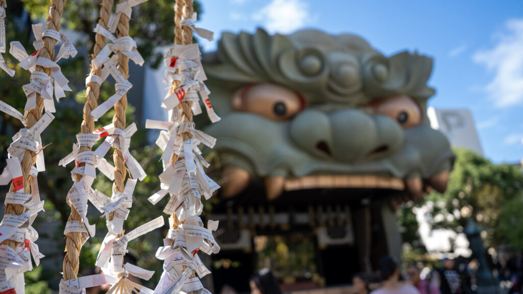 Omikuji fortunes tied to strings with the lion hall visible in the background.