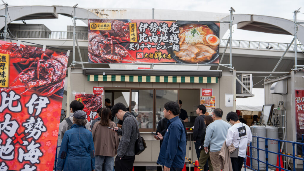 Visitors wait in line while checking their phones outside a lobster and Hinai Jidori chicken ramen booth.