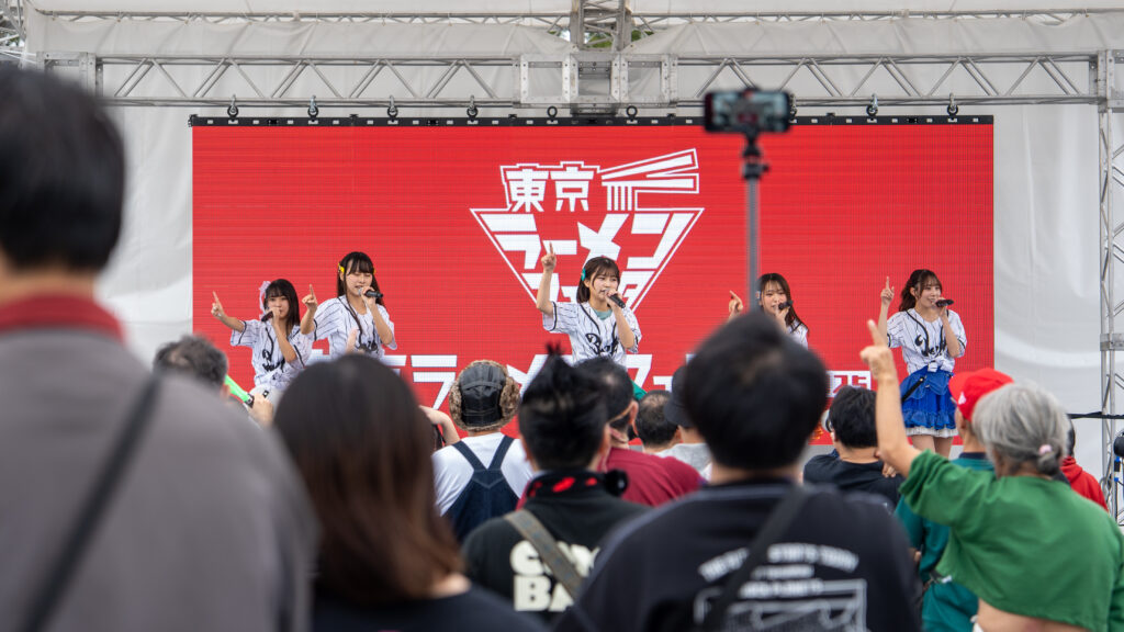 Festival performers raise one finger while an audience member mimics the gesture nearby.