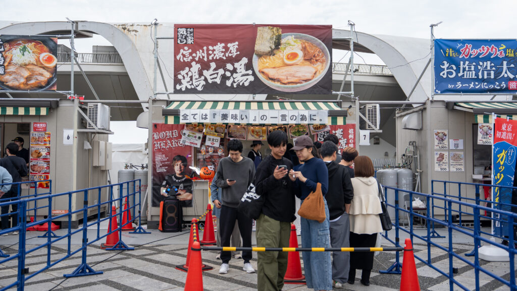 Couple studies a cellphone while waiting in line for chicken white broth ramen.