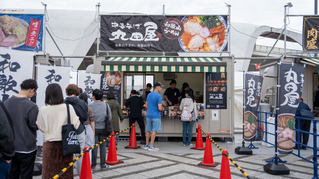Visitors wait in a long line outside the Ramen Marutaya booth serving Wakayama tonkotsu soy sauce ramen at Tokyo Ramen Festa.