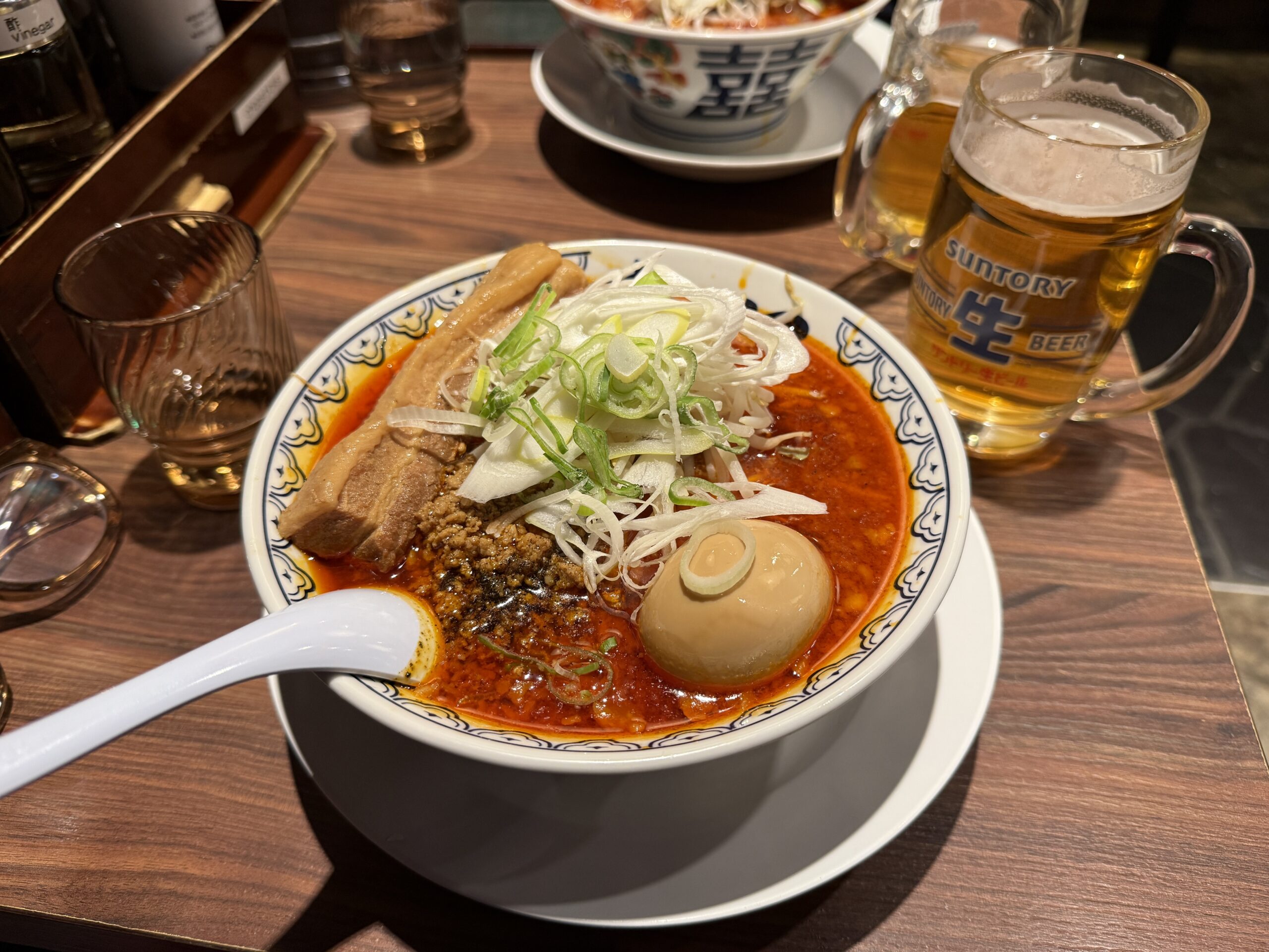 A steaming bowl of ramen with bright red broth, cabbage, sliced pork, and a halved egg on a restaurant table in Shinjuku, Tokyo.