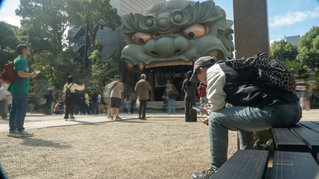 Visitors praying and taking photos in front of the lion hall at Namba Yasaka Shrine.