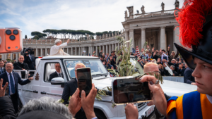 Hands holding olive branch and phone recording Pope in popemobile in St Peter’s Square