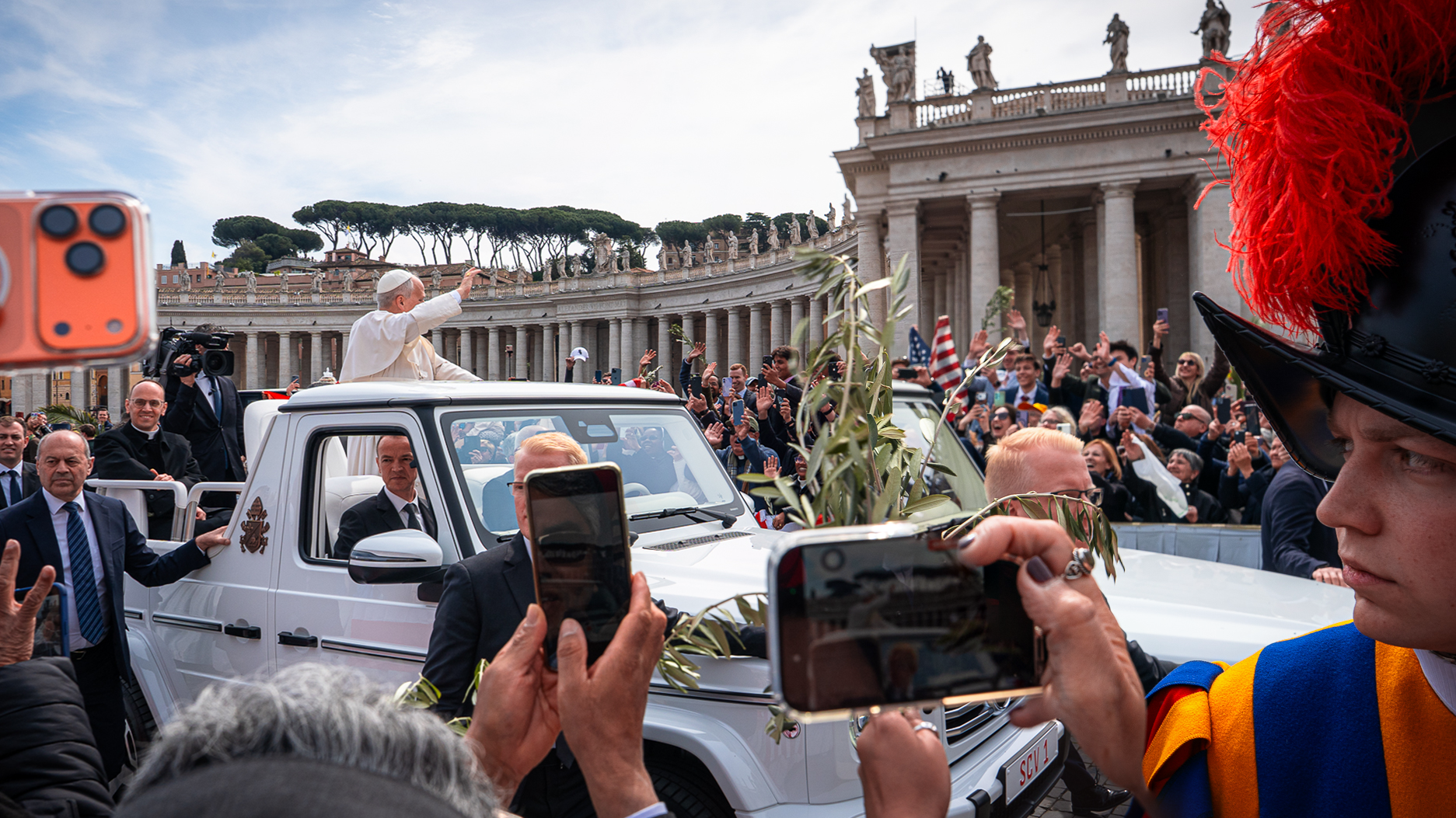 Hands holding olive branch and phone recording Pope in popemobile in St Peter’s Square