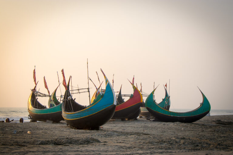 Five colorful moon boats rest on a beach along Bangladesh’s southeastern coast as the evening sky turns pink.
