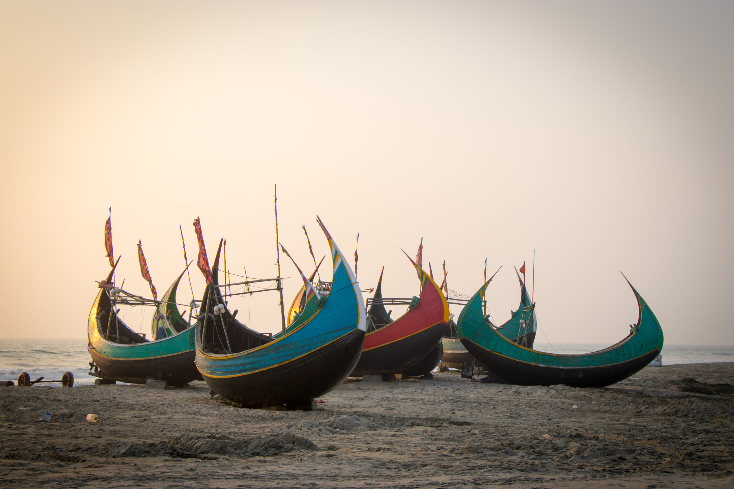 Five colorful moon boats rest on a beach along Bangladesh’s southeastern coast as the evening sky turns pink.