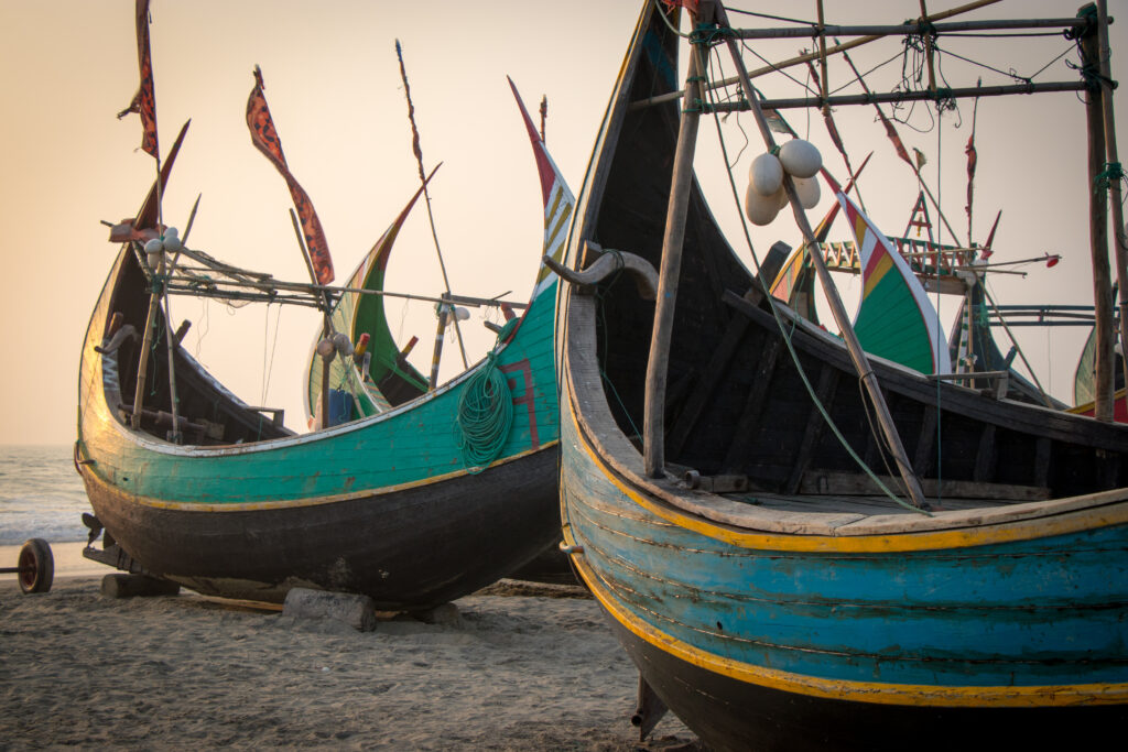 A blue moon boat with yellow trim sits in front of a bright green boat as long flags wave from their raised tips.