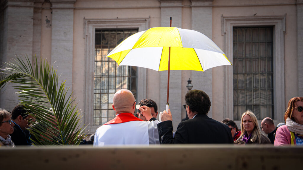 Rear view of priest offering Eucharist across aisle to worshipper in St Peter’s Square